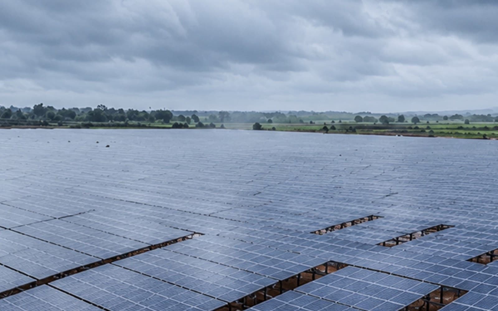 Ground-mounted solar array operating through heavy rain under storm clouds